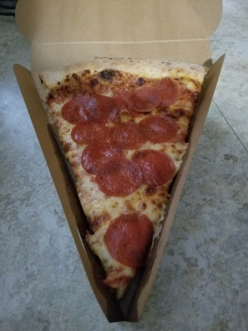 A slice of pepperoni pizza in a cardboard box, with melted cheese and crispy crust.